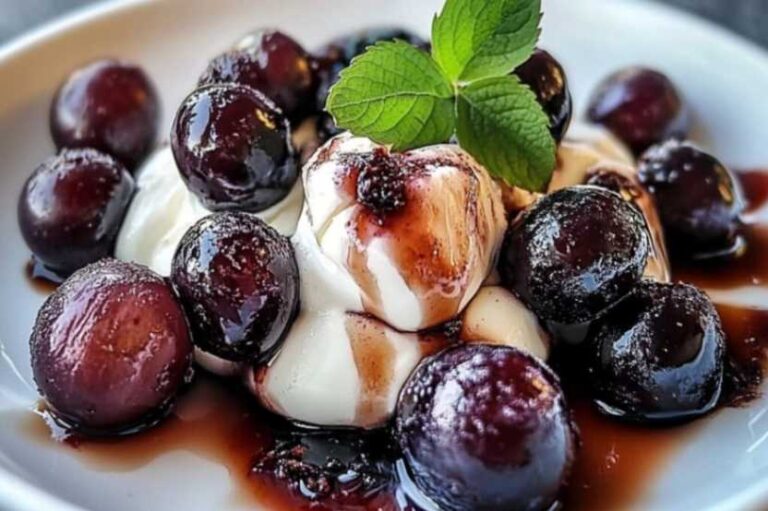 A rustic dish of sour cream burnt grapes with a golden caramelized topping, surrounded by fresh grapes and a spoon.
