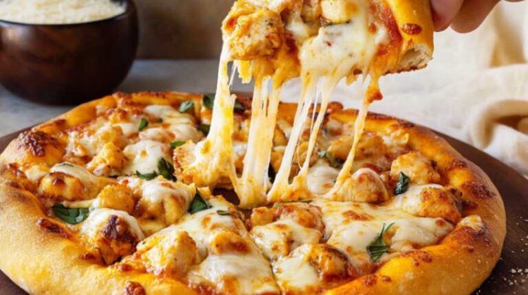 A hand pulling a cheesy slice of chicken parm pizza topped with golden chicken chunks, melted mozzarella, and fresh basil.