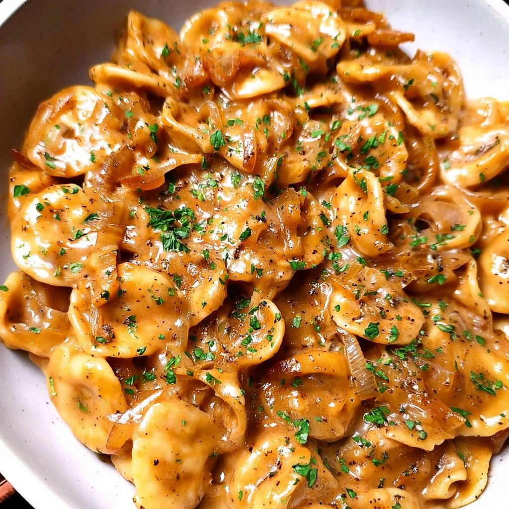 A bowl of creamy French onion pasta garnished with cheese and herbs