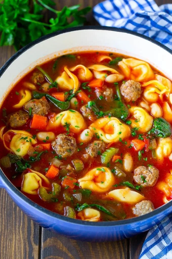 Bowl of tortellini soup with sausage garnished with herbs and cheese.