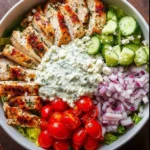 Delicious Greek Chicken Bowl topped with fresh vegetables and tzatziki sauce.