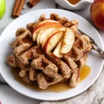 Vegan apple cinnamon waffles stacked on a plate with fresh apple slices