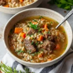 Bowl of hearty beef barley soup with vegetables and herbs