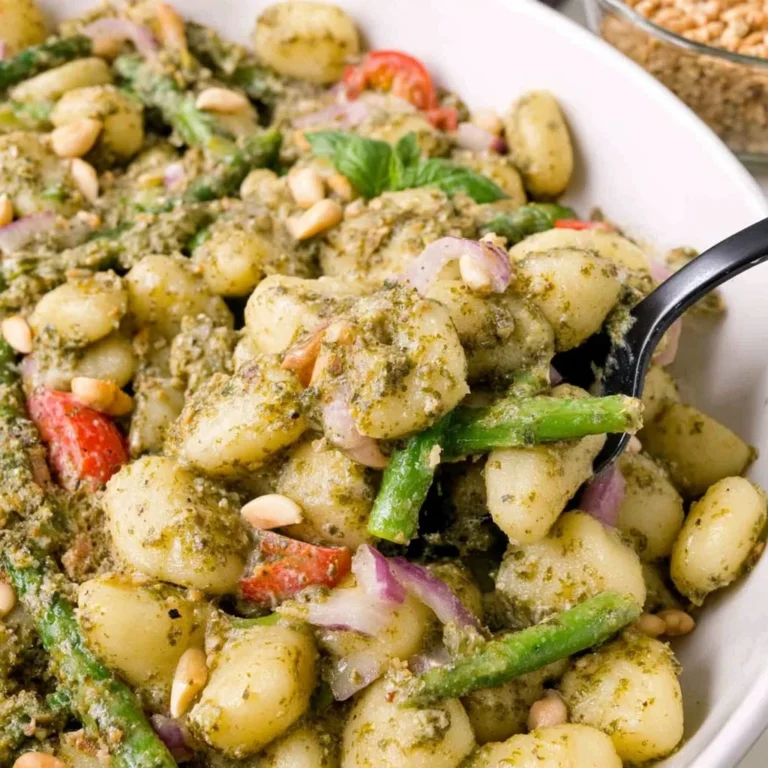 A bowl of pesto gnocchi topped with fresh basil and pine nuts.