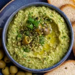 Delicious green olive dip served in a bowl with fresh herbs