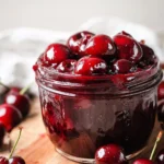 Homemade cherry sauce in a glass jar with fresh cherries