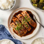 Plate of delicious teriyaki salmon garnished with green onions and sesame seeds.
