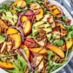 Vibrant grilled peach salad with greens and feta cheese on a plate.