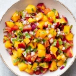 Bowl of fresh peach salsa with colorful ingredients displayed