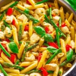 A plate of Asiago Chicken Pasta garnished with herbs and served with a side of garlic bread.