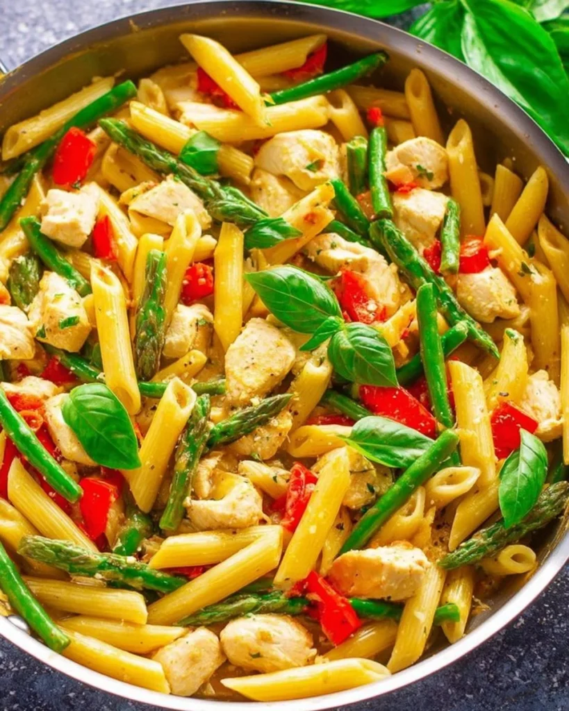 A plate of Asiago Chicken Pasta garnished with herbs and served with a side of garlic bread.