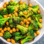Cheesy roasted broccoli and chickpeas served in a bowl, garnished with herbs.