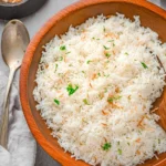 Bowl of Coconut Rice garnished with fresh herbs and served with tropical fruits