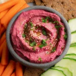 Bowl of vibrant and creamy beet hummus with fresh vegetables and pita