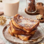Plate of delicious Eggnog French Toast topped with powdered sugar and syrup.