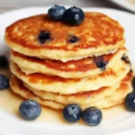 Fluffy protein pancakes stacked on a plate, drizzled with maple syrup.