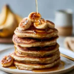Delicious vegan plantain pancakes stacked on a plate with fresh fruit