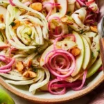 Apple and fennel salad topped with pickled onions and almonds on a plate