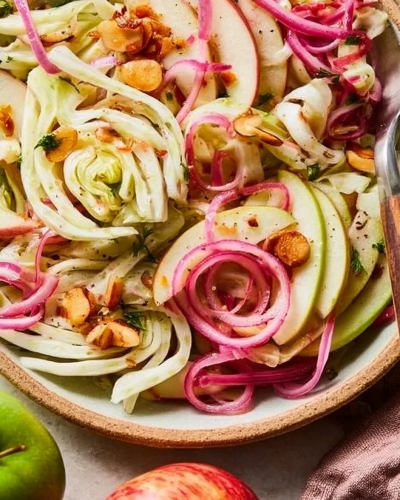 Apple and fennel salad topped with pickled onions and almonds on a plate